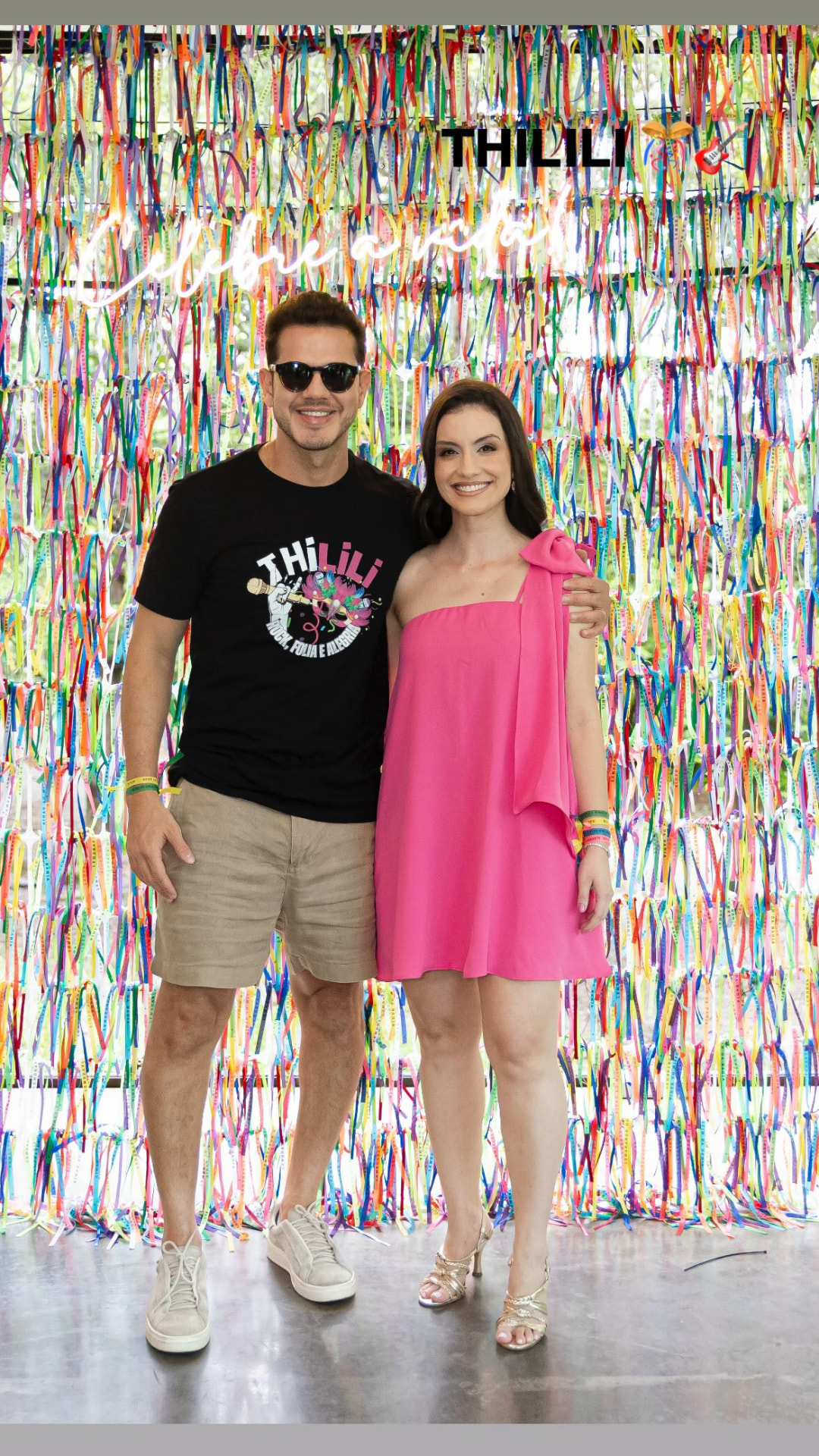 Casal aniversariante posando em frente a painel de fitas coloridas