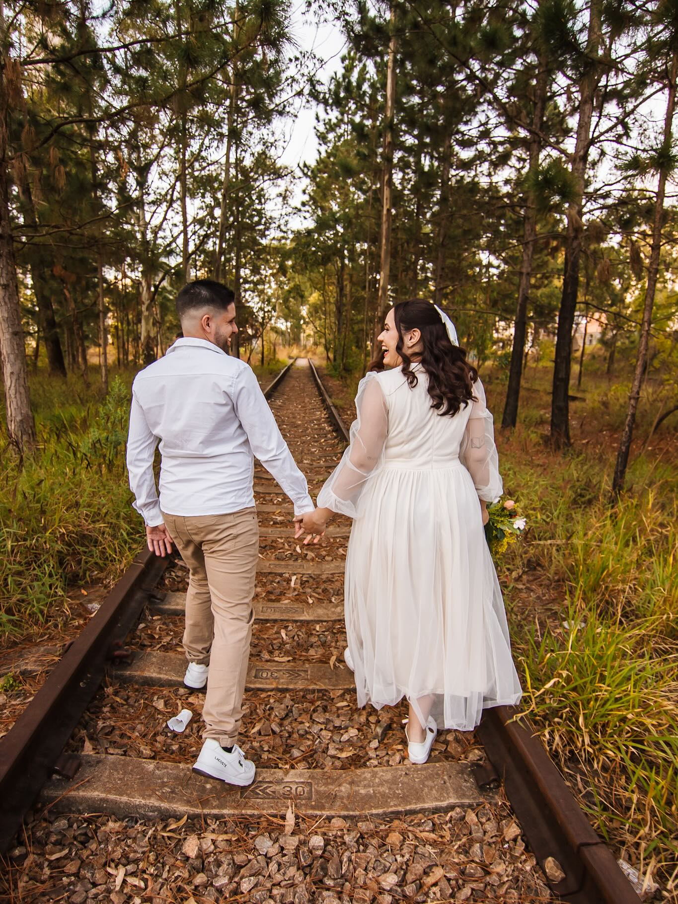 Casal de mãos dadas caminhando sobre trilhos em ensaio pré-wedding