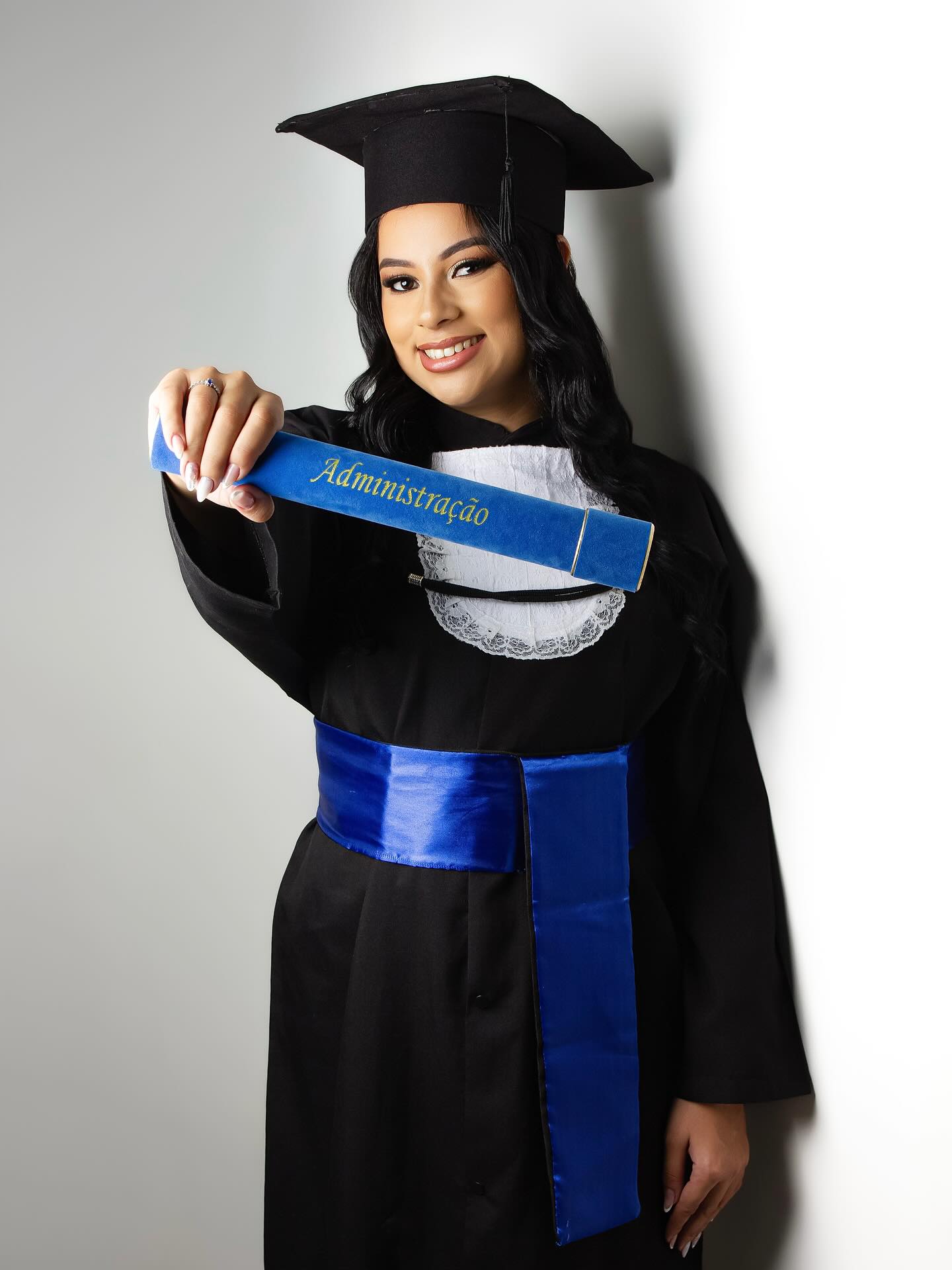 Formanda de beca e capelo segurando diploma de Administração