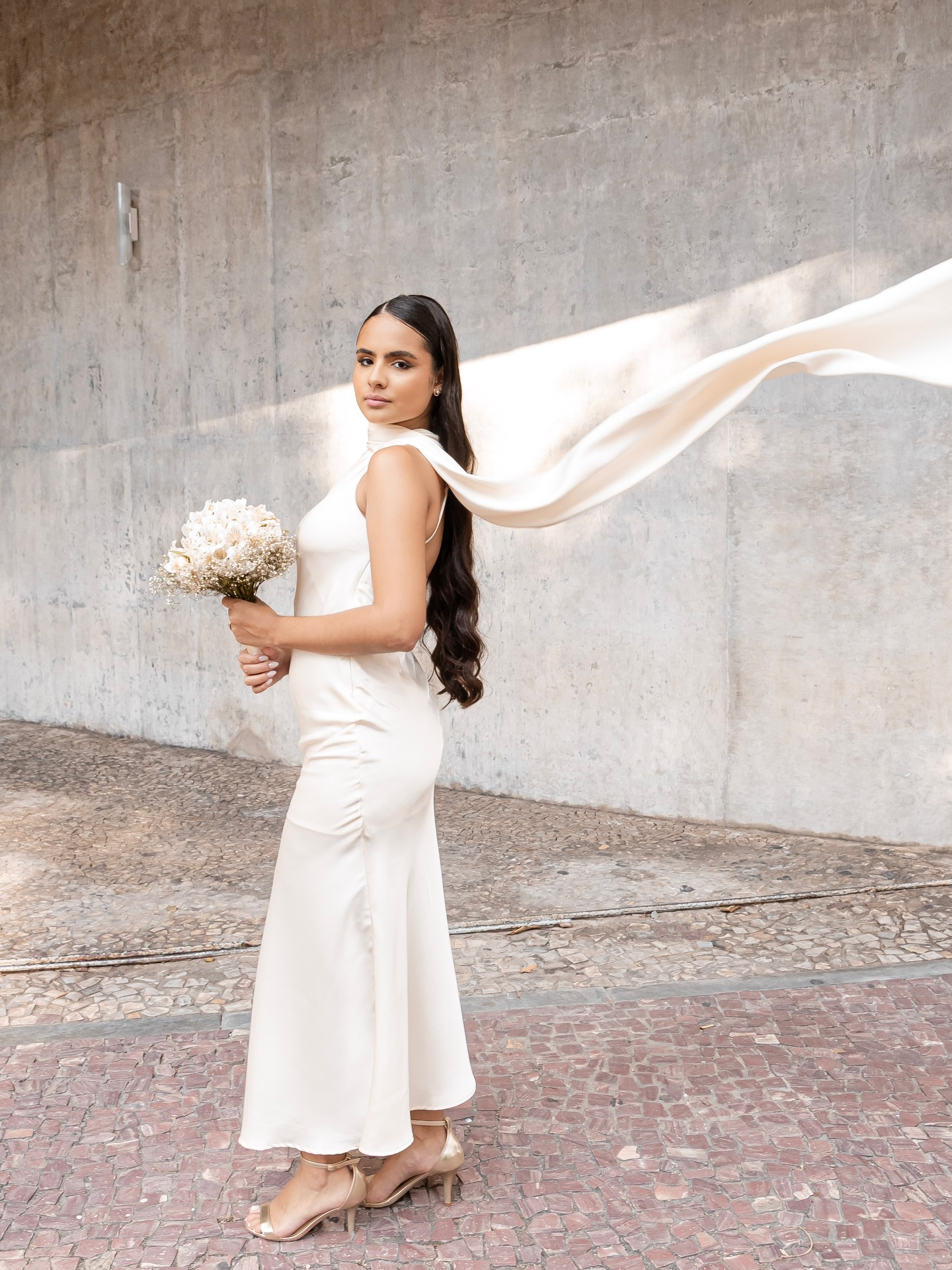 Noiva de vestido de cetim com buquê e véu ao vento após o casamento civil